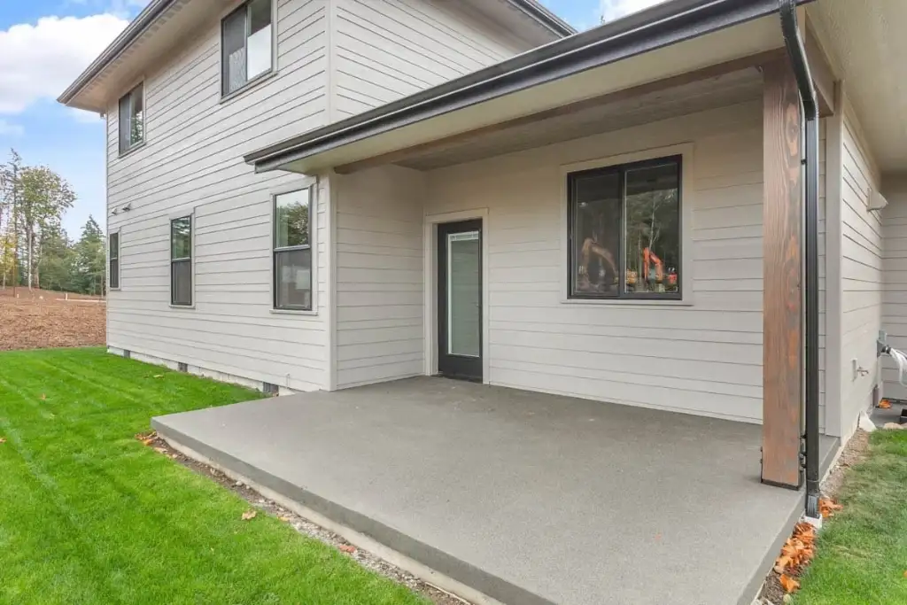 The 15-by-15-foot covered rear patio of plan 280263JWD with a wood-wrapped post, a glazed back door and a broad concrete slab