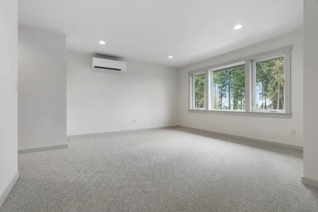 The 20-by-15-foot bonus room over the garage in plan 280263JWD, carpeted, with a bank of windows and a ductless mini-split head