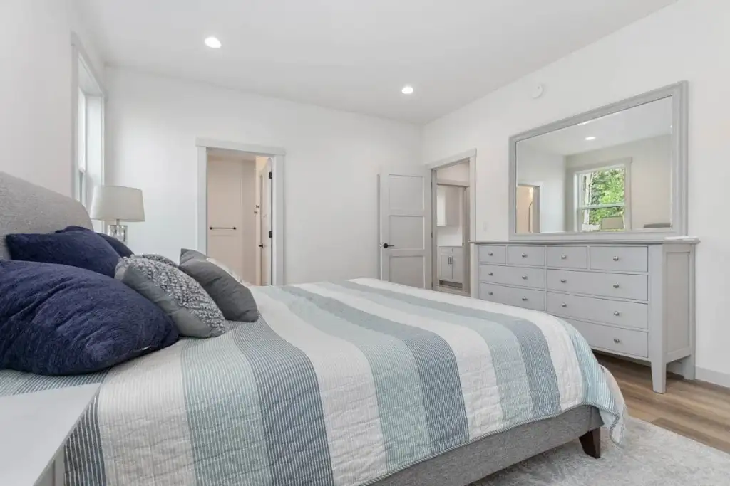 Main-level master bedroom of plan 280263JWD staged with a bed, dresser and doors to the walk-in closet and ensuite bathroom
