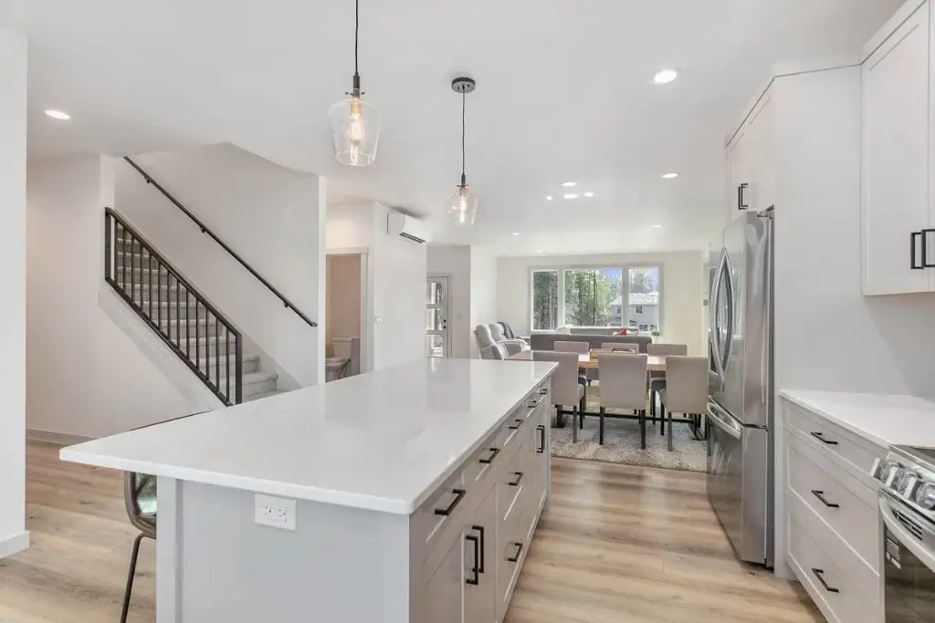 Kitchen island in plan 280263JWD looking toward the dining and living rooms, with the stair and its black metal balusters at left