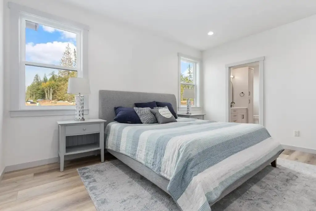 Main-level master bedroom in plan 280263JWD with two windows, wood-look flooring and a doorway into the ensuite