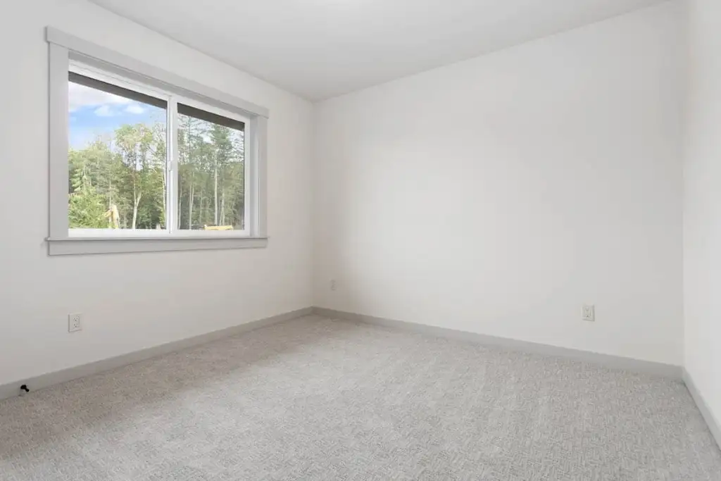 Carpeted secondary bedroom in plan 280263JWD with a slider window looking into the trees