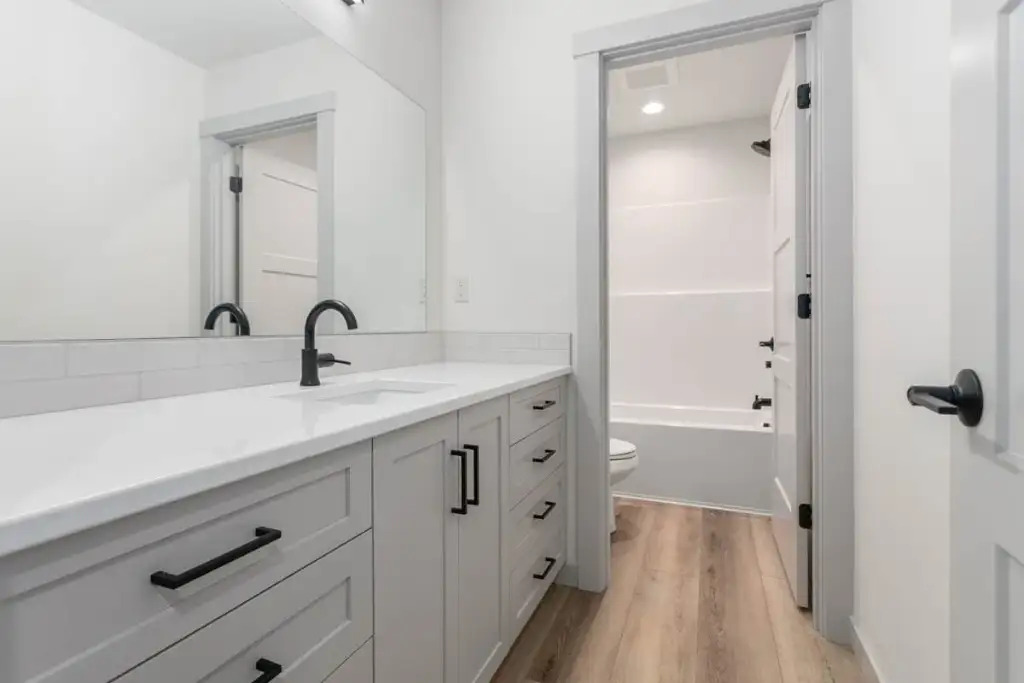 Upstairs shared bathroom in plan 280263JWD with a long vanity, black fixtures, subway tile and a separate tub and toilet compartment