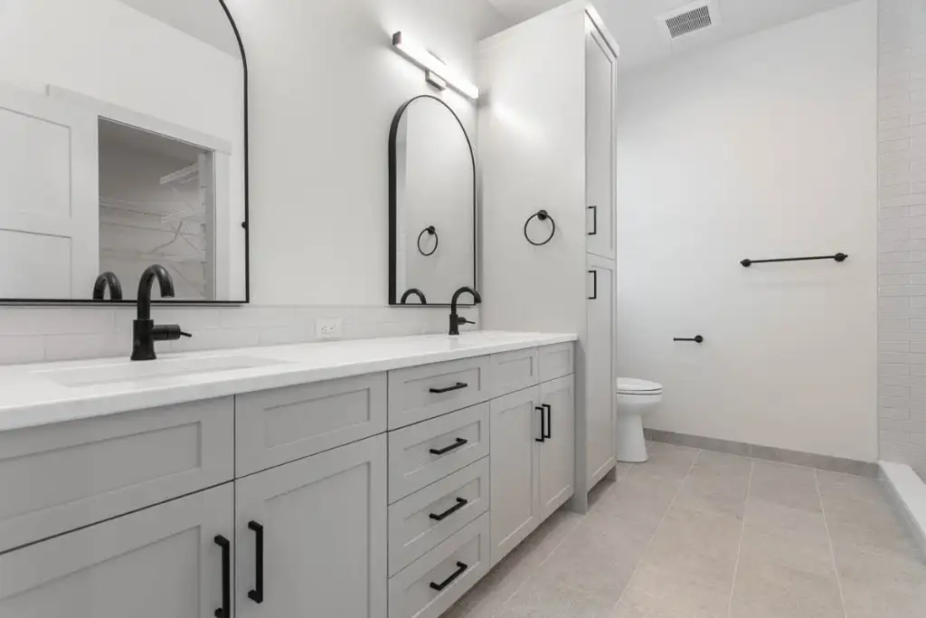 Master bathroom in plan 280263JWD with a double vanity, arched black mirrors, a linen tower, tiled floor and a separate toilet area
